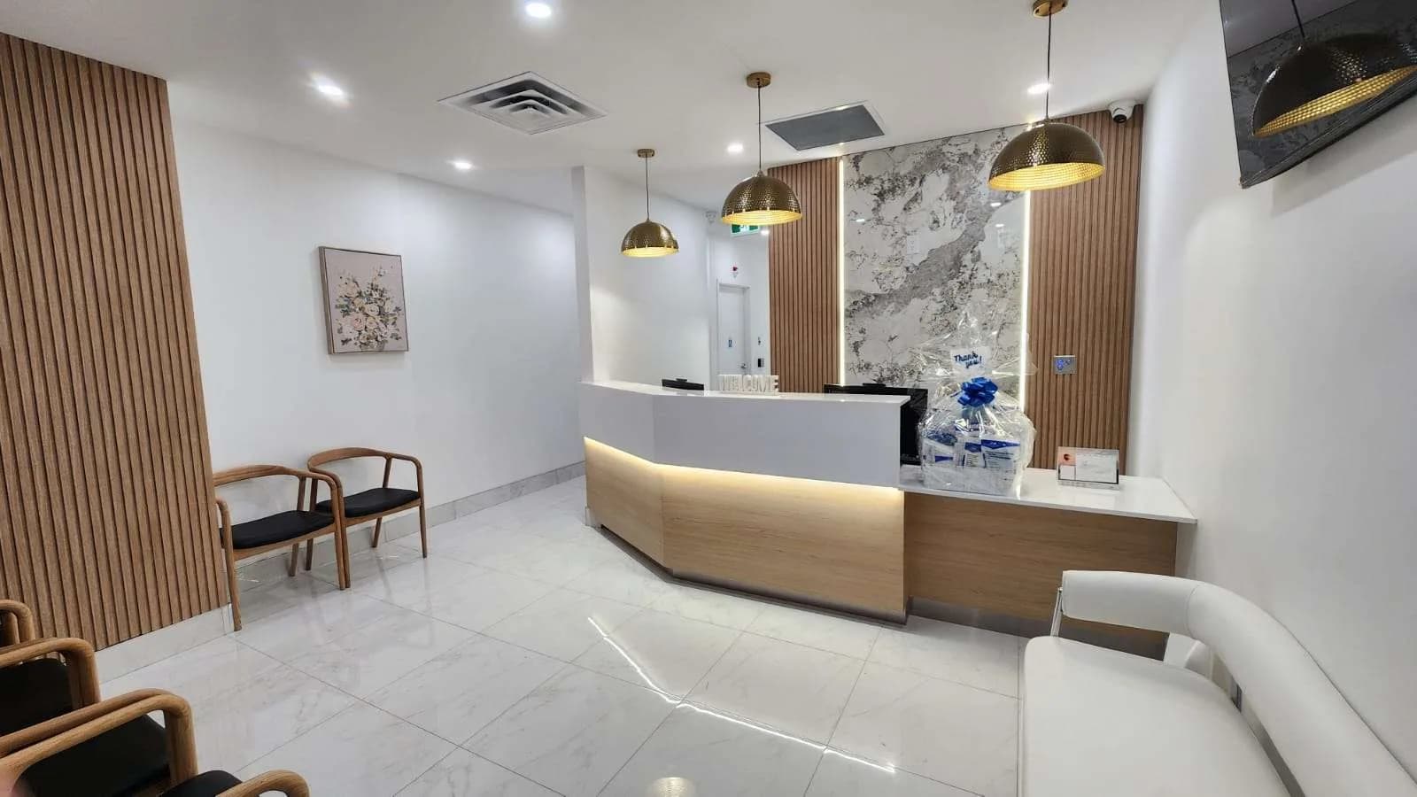 The bright reception and waiting area at Janood Dental in Etobicoke, with a curved front desk and comfortable seating